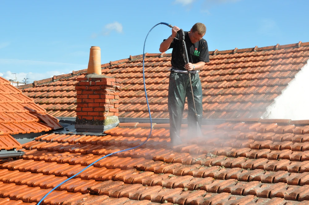 Homme effectuant le nettoyage haute pression d'une toiture en tuiles terre cuite
