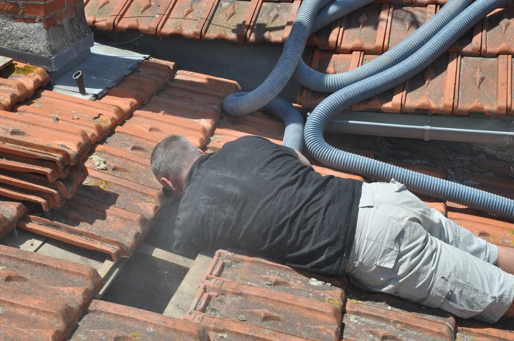 Technicien en combinaison de travail intervient sur toiture en tuiles terre cuite