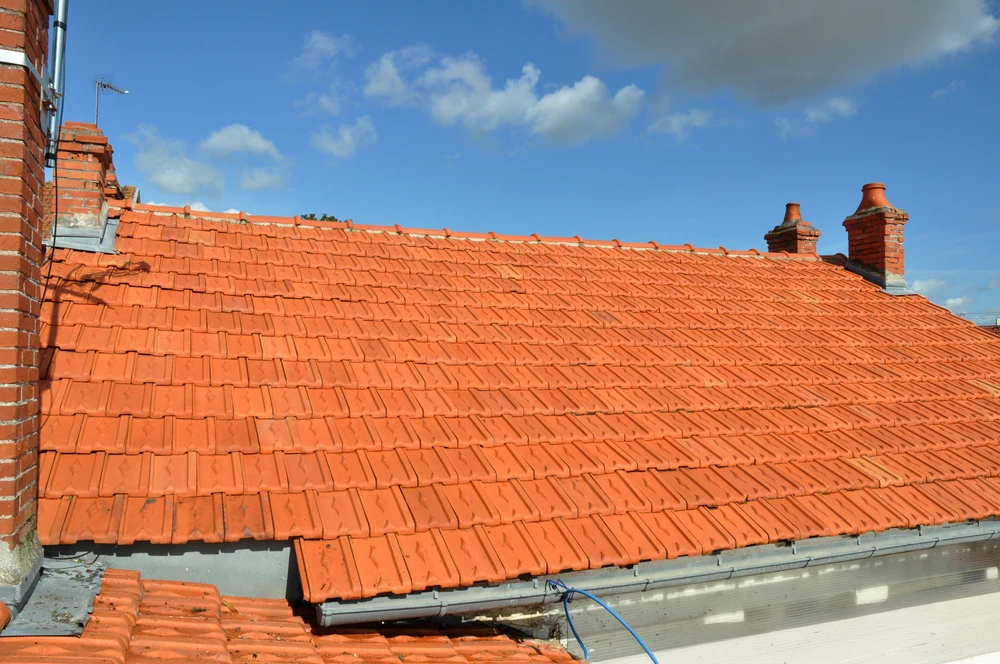 Chantier de rénovation de toiture en extérieur avec ouvriers installant des tuiles terre cuite rouge sur charpente