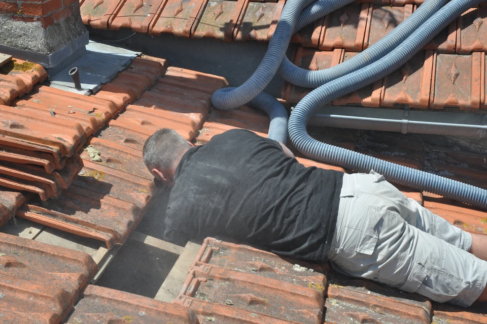 Chantier de construction en extérieur, ouvrier en pull rayé bleu et blanc installant une membrane d'étanchéité sur toiture inclinée